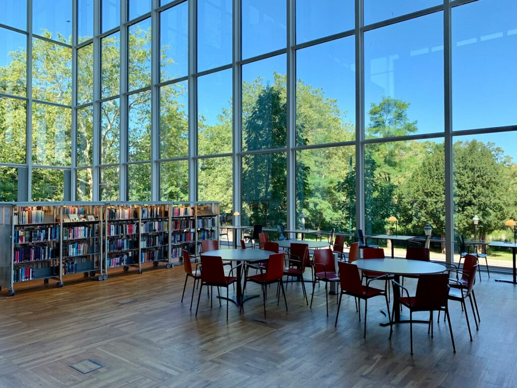 Bibliothek mit großen Fensterfronten, Bücherregalen und Arbeitstischen mit Blick ins Grüne