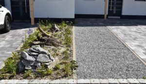 Vergleich zwischen naturnah gestalteter Fläche mit Pflanzen und konventionell geschotterter Fläche vor einem Gebäude