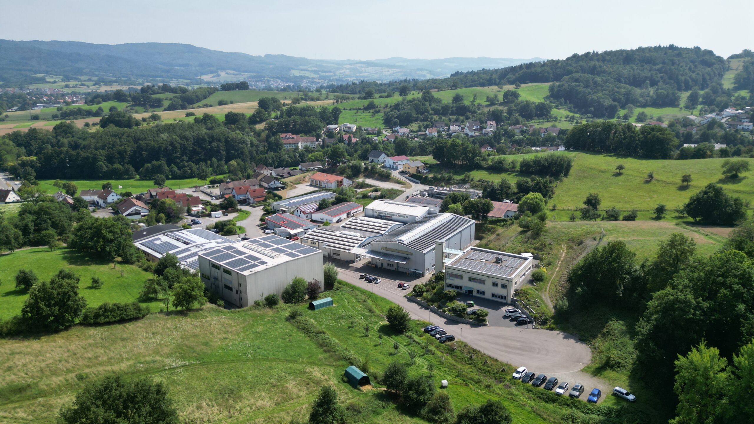 Drohnenaufnahme des Firmengeländes der SPIR STAR AG in einer grünen, hügeligen Landschaft.
