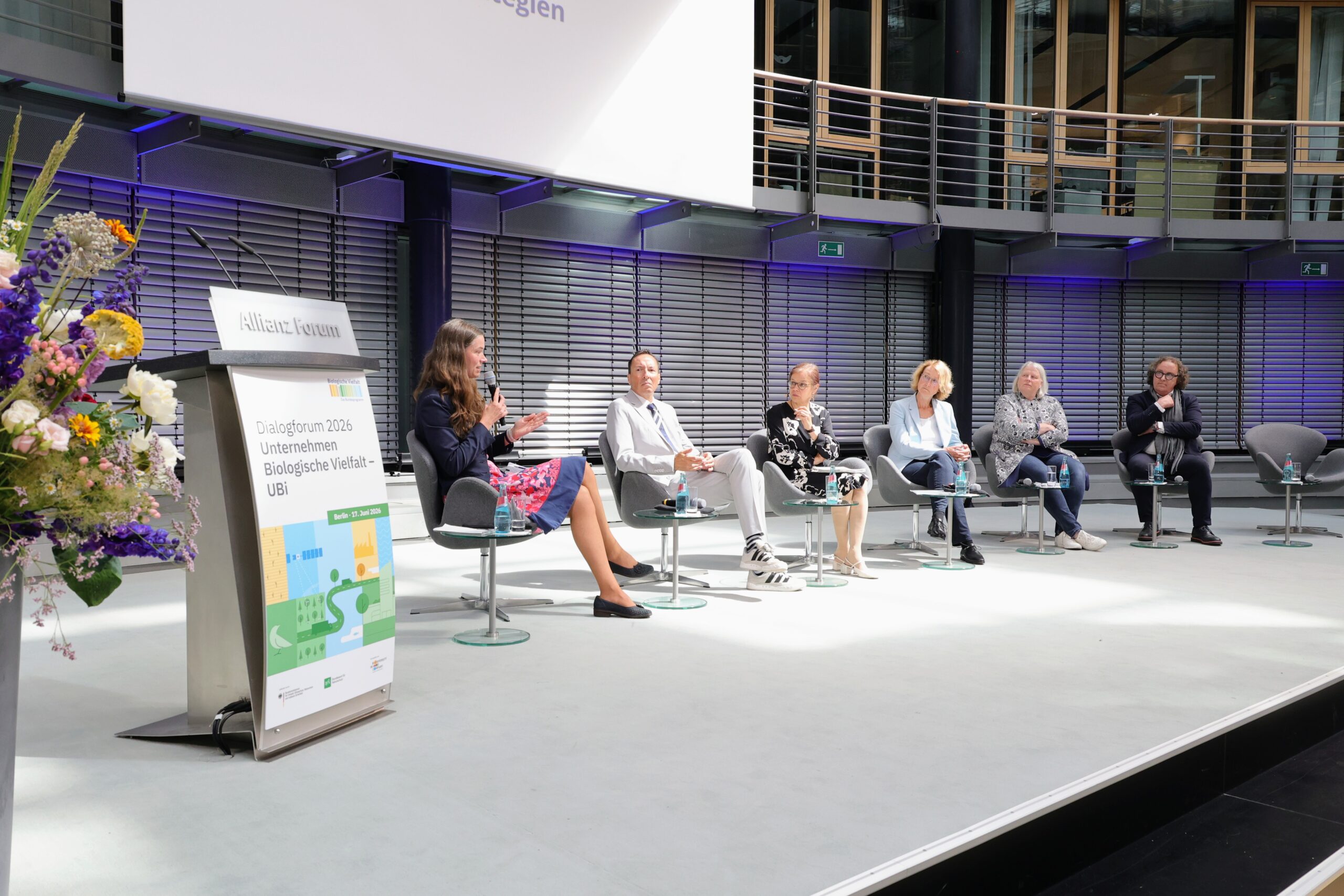 Podiumsdiskussion beim UBi-Dialogforum 2026 im Allianz Forum Berlin mit Moderatorin und Teilnehmenden auf der Bühne.