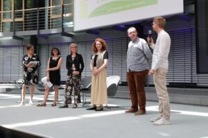 Moderatorin Dr. Tanja Busse steht mit Veronica Veneziano, Louisa Lösing, Eva Baumgärtner, Sven Schulz und Oliver Peters beim UBi-Dialogforum 2026 auf der Bühne.